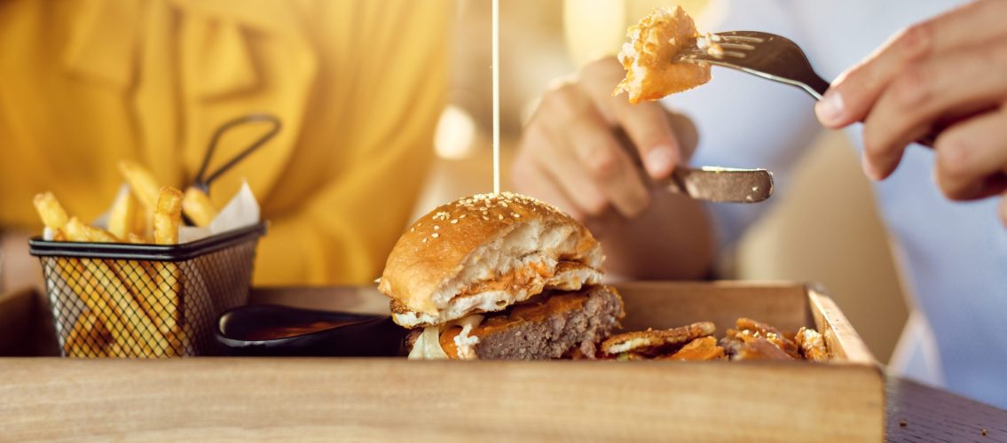 Close-up of couple having cheeseburger and French fries for lunch in a restaurant.